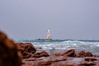 撒丁岛岩石海岸上，灯塔被碧绿海浪包围的景色十分壮丽