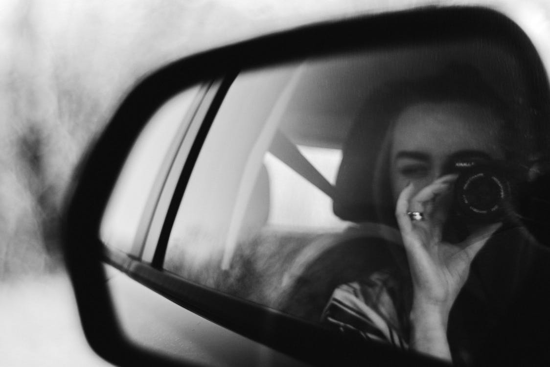 無料 車のサイドミラーでカメラ撮影を保持している女性のグレースケール写真 写真素材