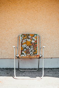 一把带有鲜艳花卉图案的空复古椅子靠在纹理墙壁上，展现出复古风格