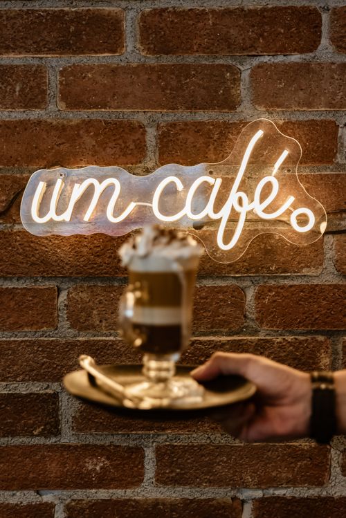 Free A barista presents a mocha on a tray against a brick wall adorned with neon signage. Stock Photo