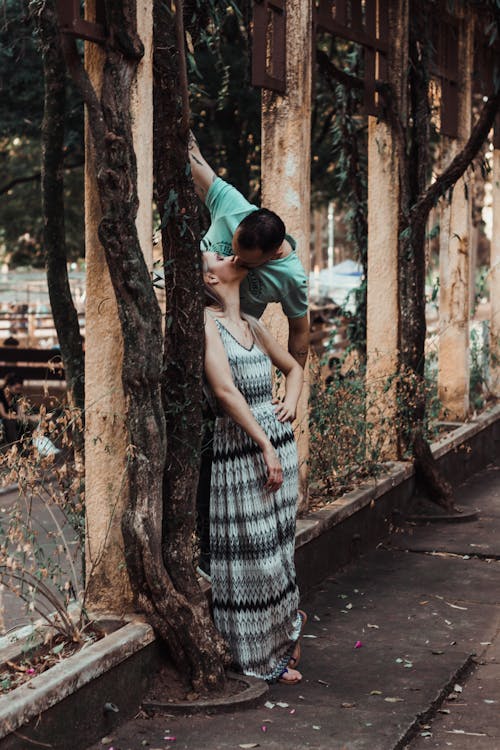 Man Kissing Woman Who Is Leaning Against Tree