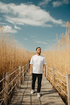 A man walks along a boardwalk through tall grass in Sultansazı, Türkiye under a blue sky.
