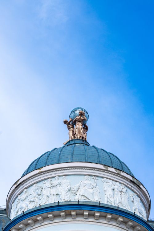 Free A bronze statue atop an elaborate dome under a vibrant blue sky, showcasing architectural elegance. Stock Photo