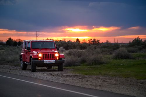 Free A red Jeep parked beside a rural road at sunset, with a striking sky in the background. Stock Photo