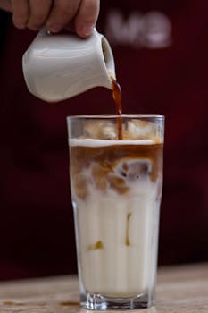 Close-up of espresso being poured into iced latte with milk, creating a delicious cold coffee drink.