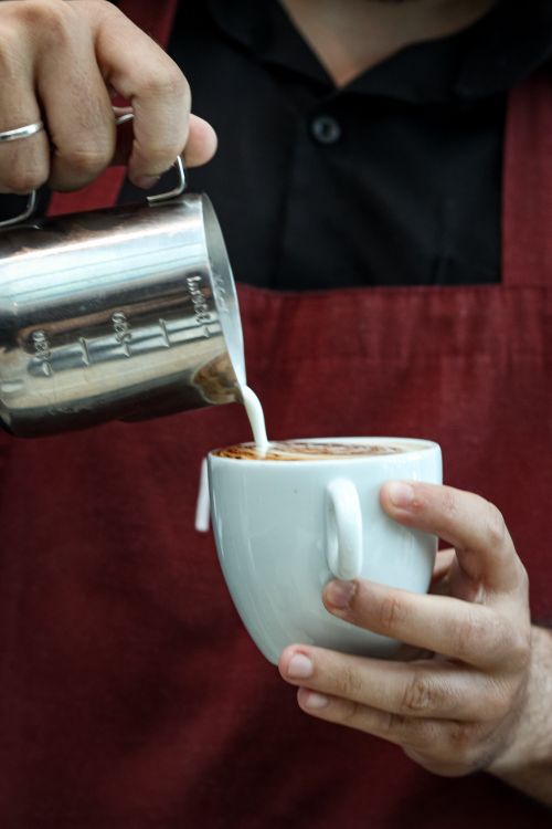 Free Close-up of a barista creating latte art by pouring milk into a cappuccino. Stock Photo