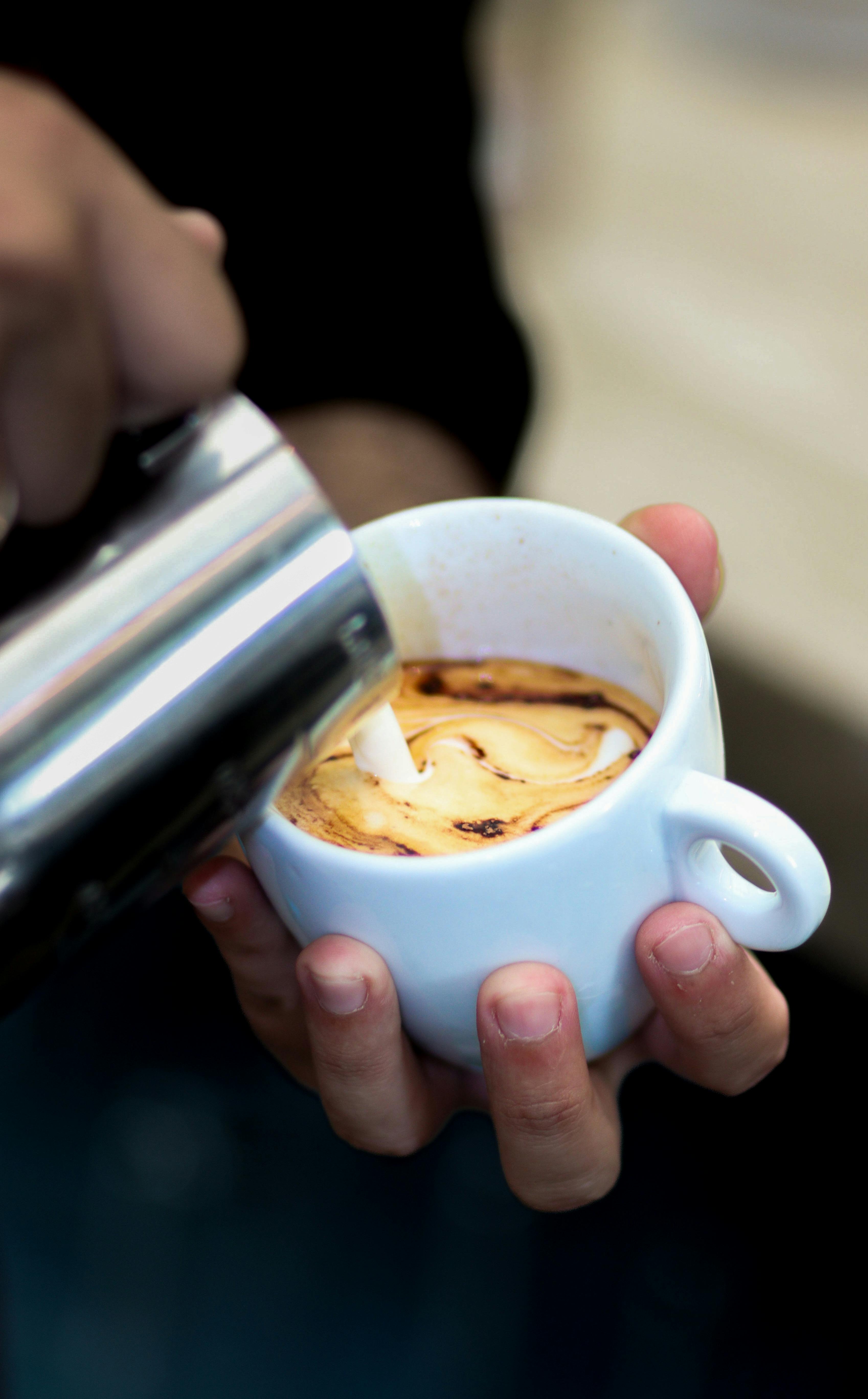 Mano de barista vertiendo latte art con precisión