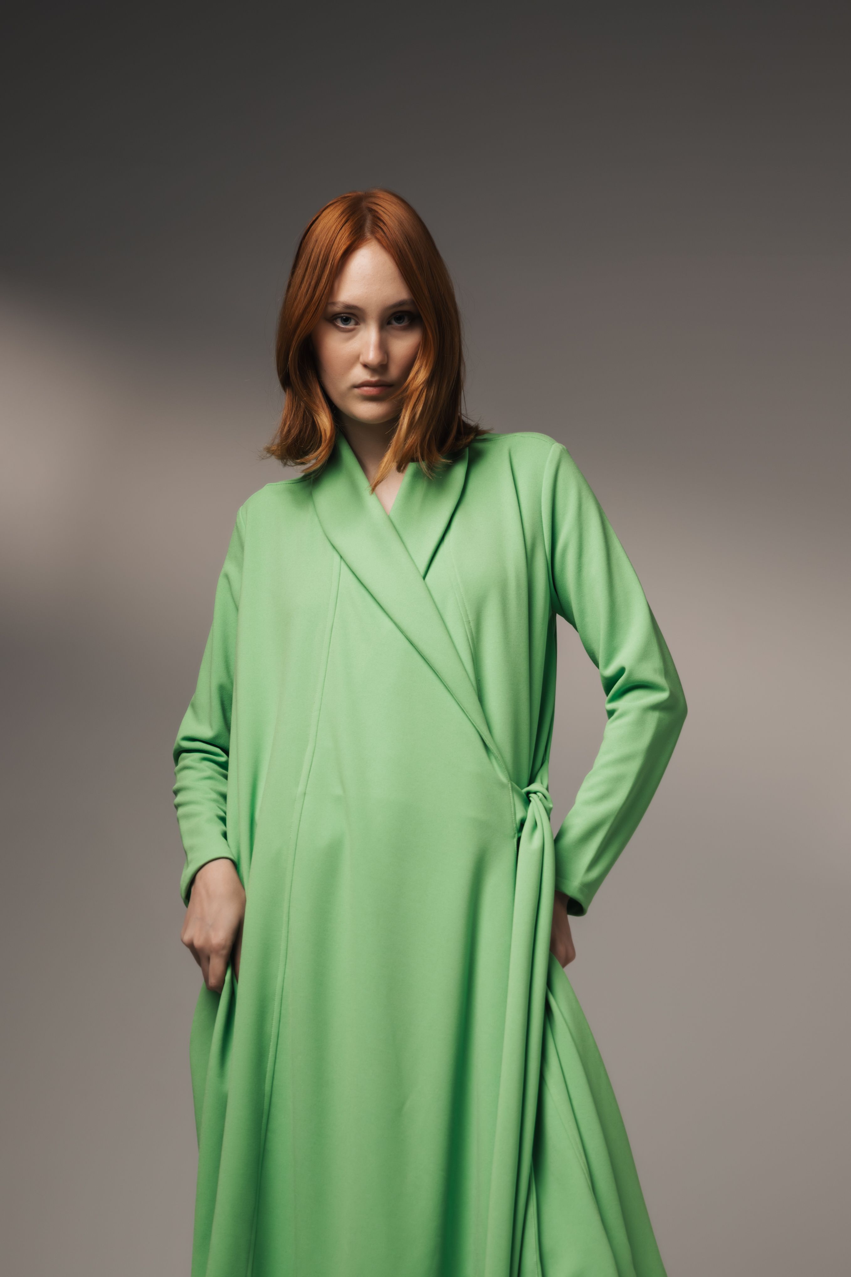 Retrato de moda de uma mulher em um robe verde fluido posando em um estúdio.