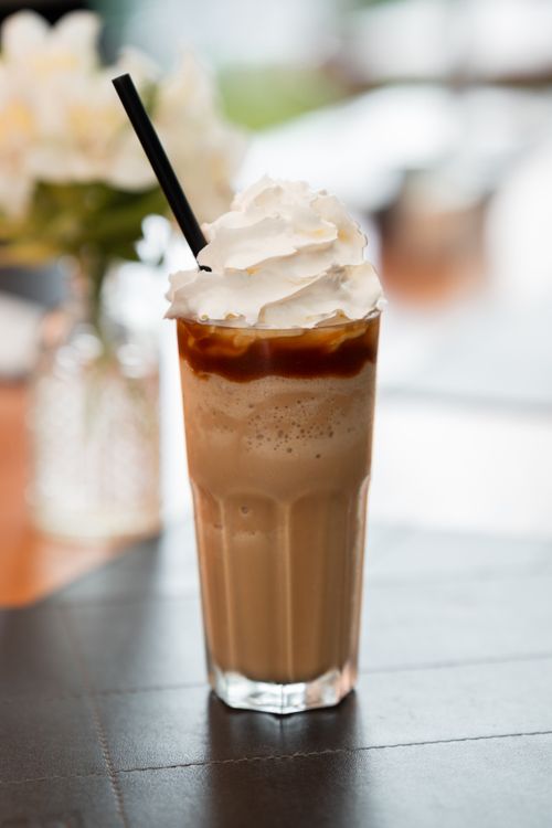 Free Tall glass of iced coffee topped with whipped cream and caramel sauce, featuring a straw in a cafe setting. Stock Photo