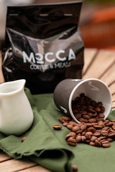 High-quality roasted coffee beans spilling from a cup with MECCA Coffee & Meals branding.