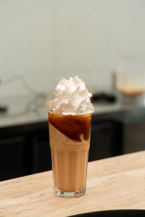 Free Tall glass of iced coffee topped with whipped cream on a wooden table, perfect for a refreshing treat. Stock Photo