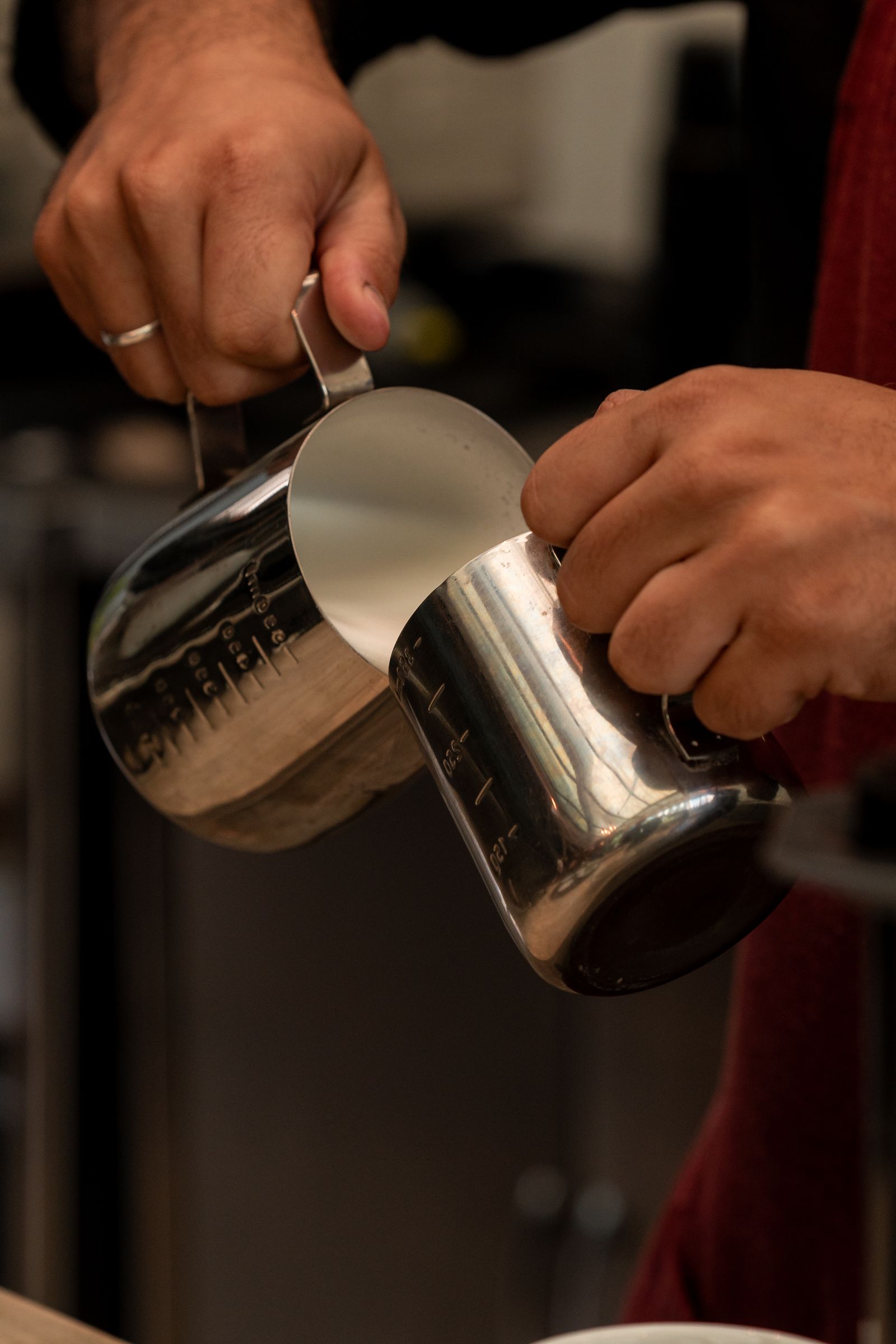 Barista holding two unbranded stainless-steel milk pitchers by their handles