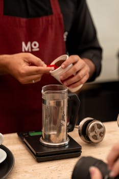 Close-up of a barista measuring coffee for brewing with a French press.