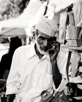 一名年长男子穿着传统服装，在户外市场打电话