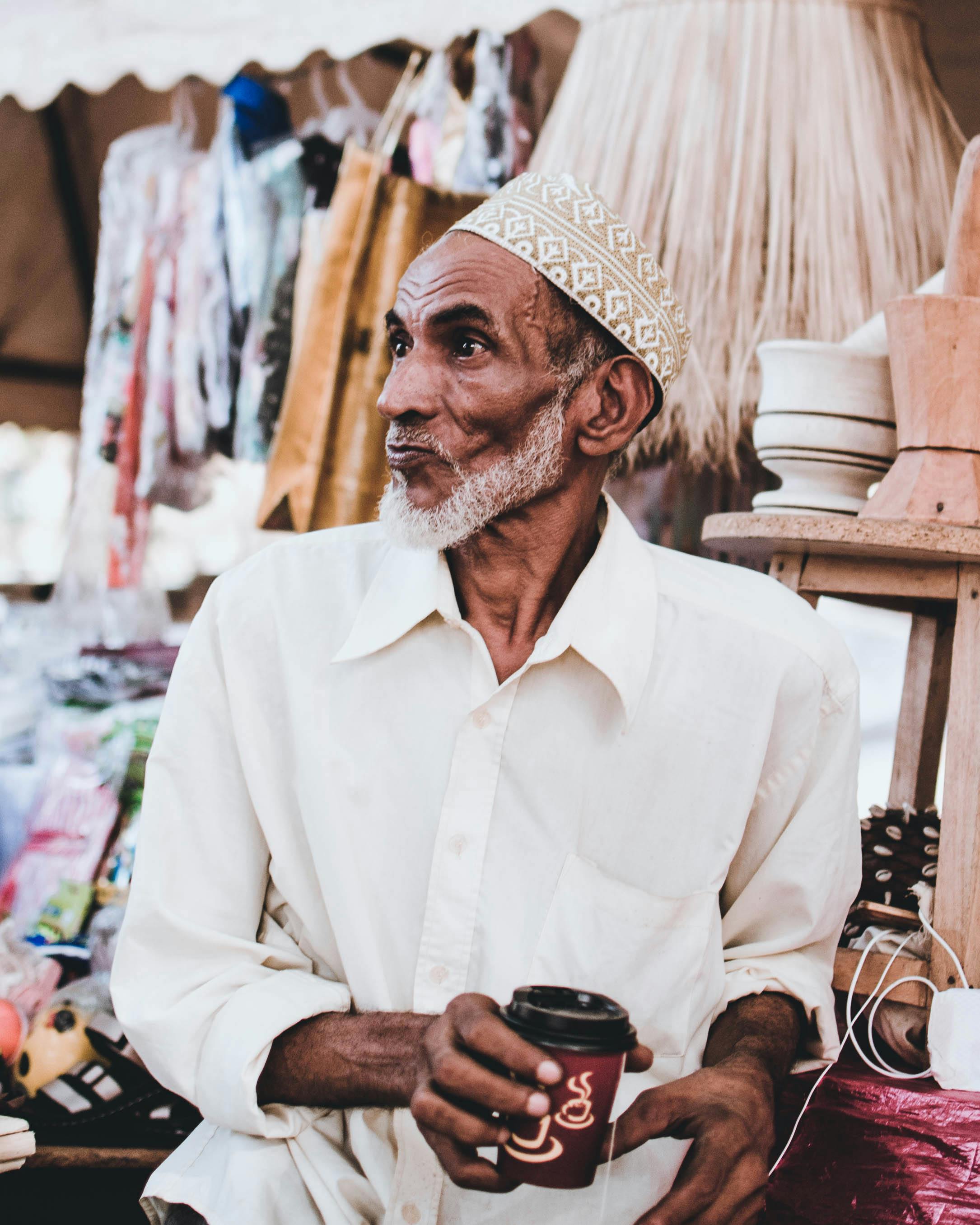 一位年长的商人拿着咖啡杯，走在充满活力的街头摊位市场上