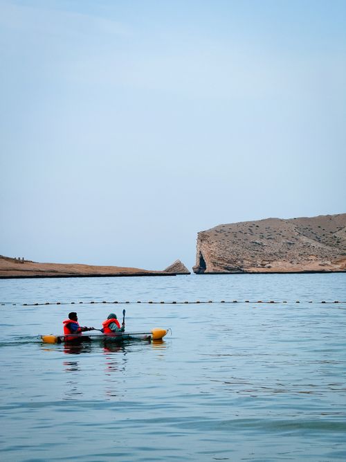Free Two people kayaking in the serene coastal waters of Oman, near a rocky cliff. Stock Photo