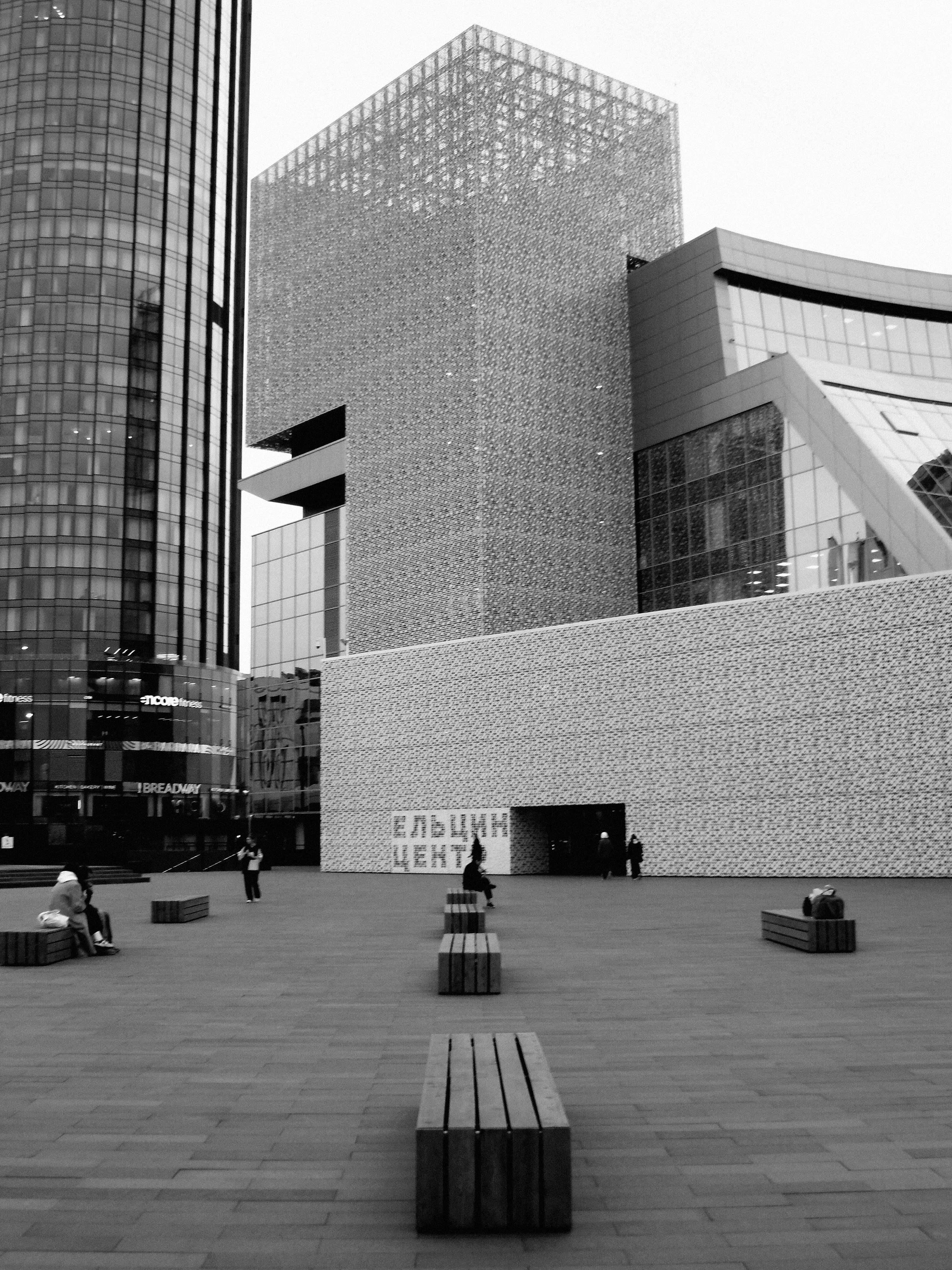 Black and white photo of Yeltsin Center in Yekaterinburg with people and benches in the town square.