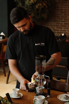 A barista prepares coffee with a siphon brewer in a cozy café setting, illustrating a unique coffee-making process.