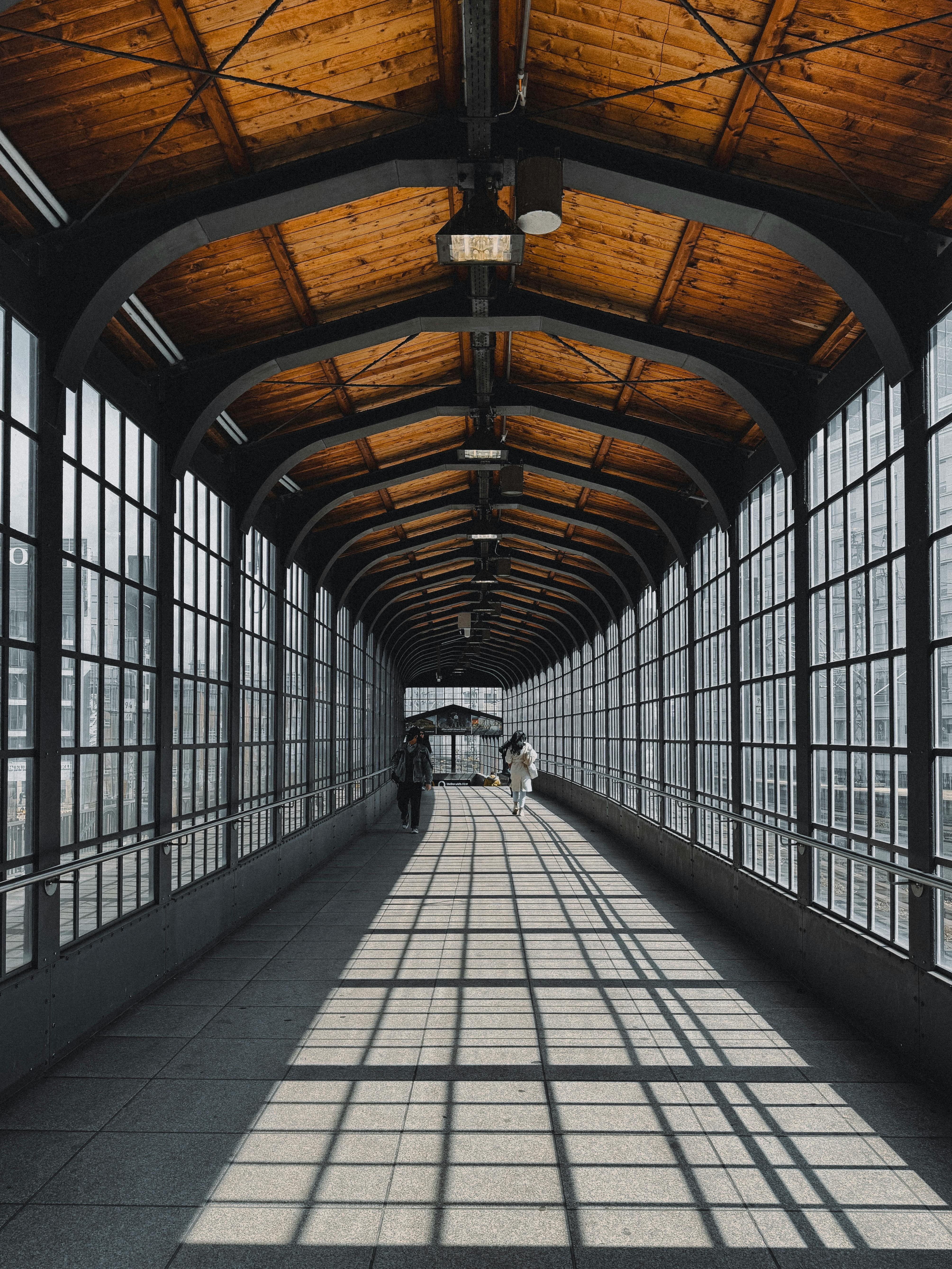 A glass tunnel in Berlin with people walking and sunlight casting patterns.