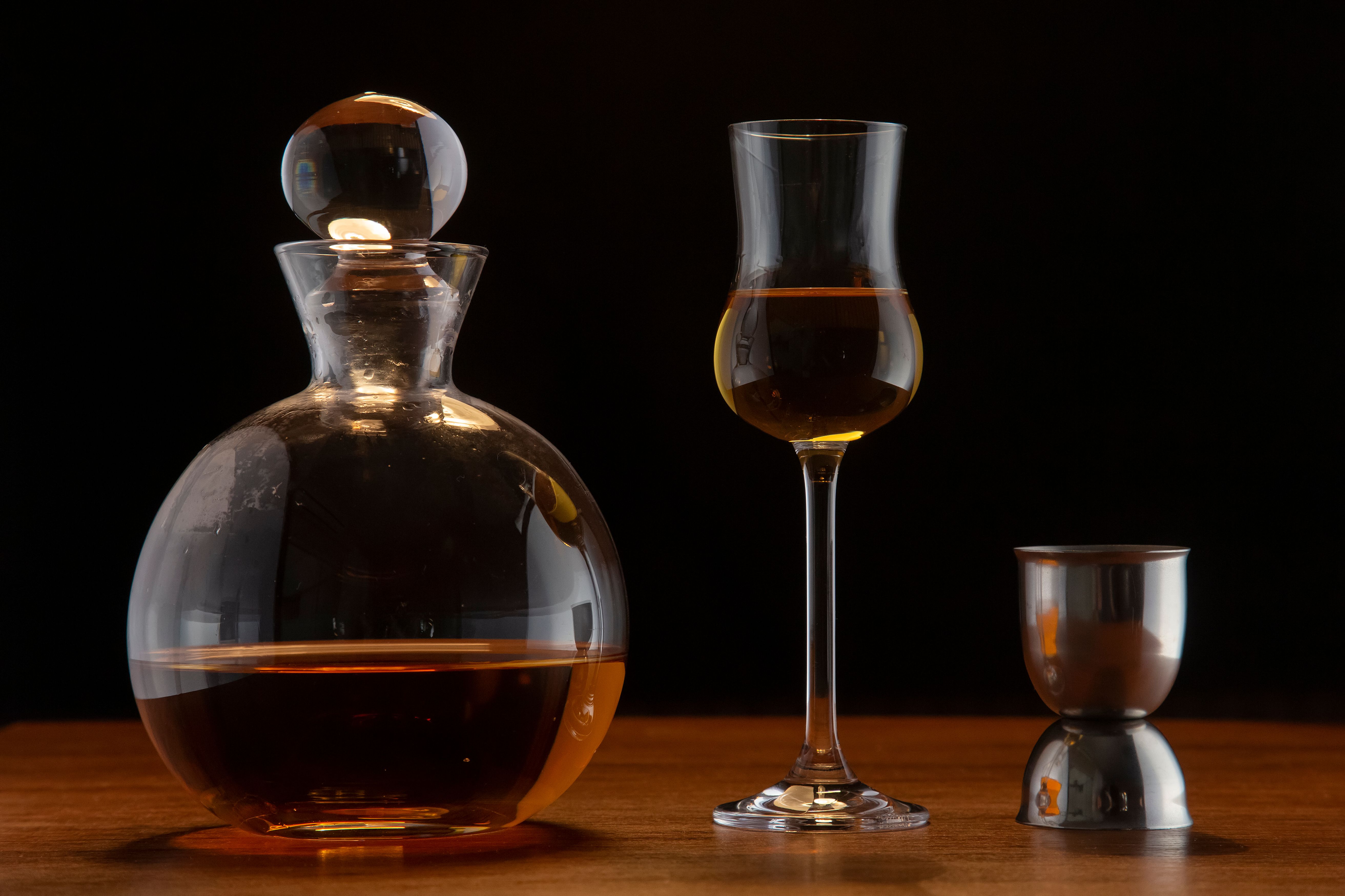 Elegant still life with a whiskey decanter, glass, and jigger on wooden surface.