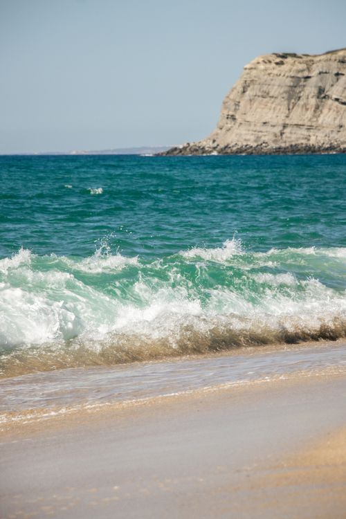 Free Energetic ocean waves crash against a rocky shore under clear sky, capturing the essence of nature's power. Stock Photo