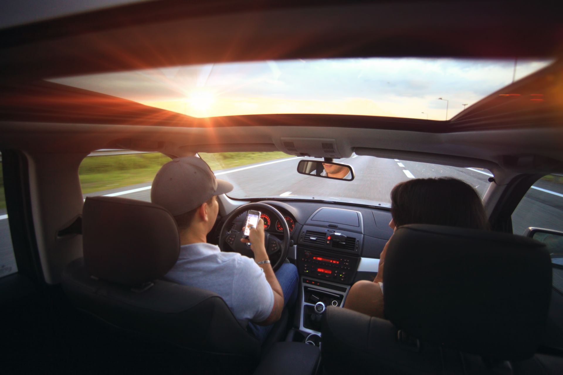 Driver using phone while driving at sunset with passenger in vehicle.