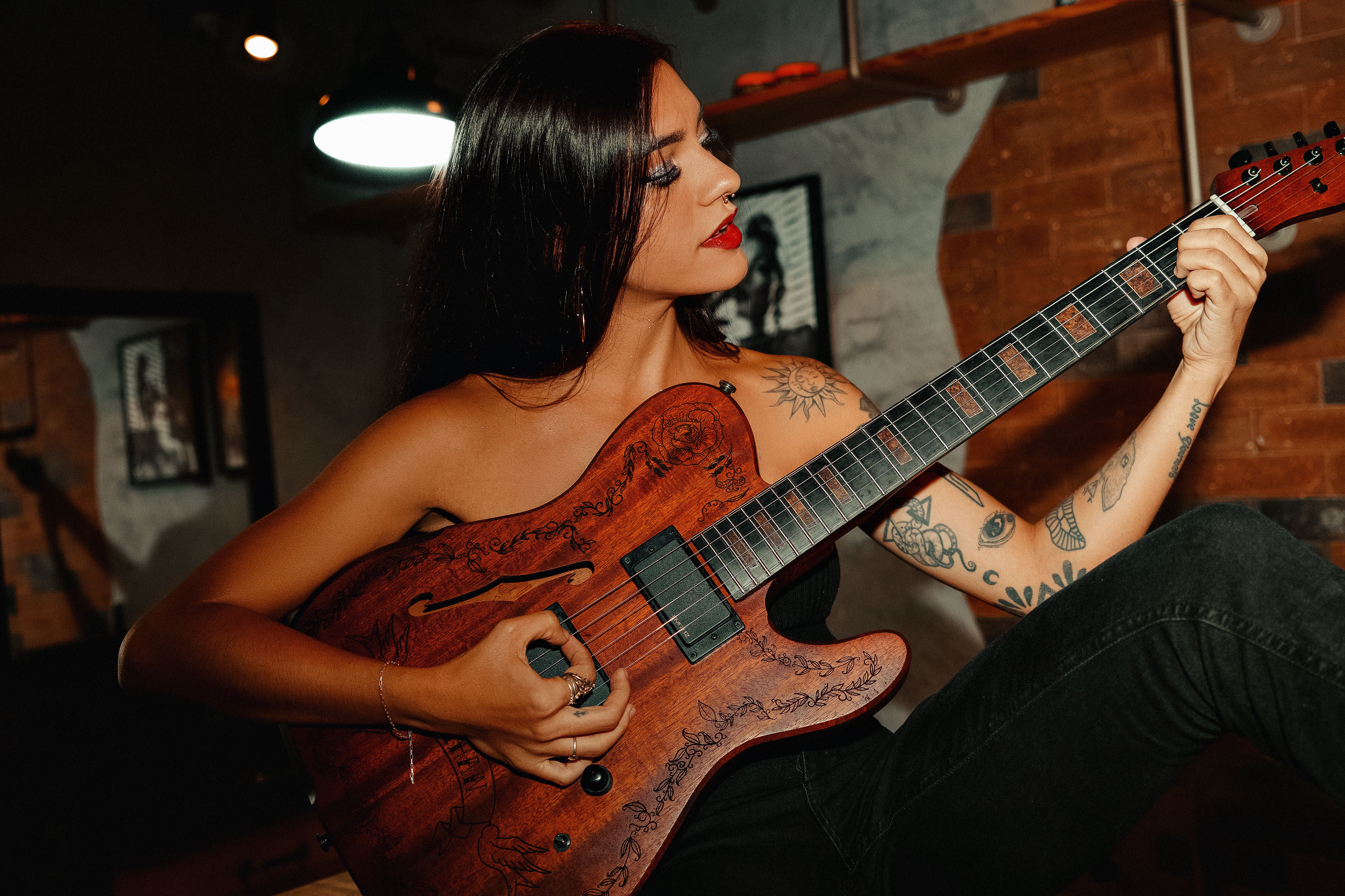Woman with tattoos plays an electric guitar with focus and passion indoors.