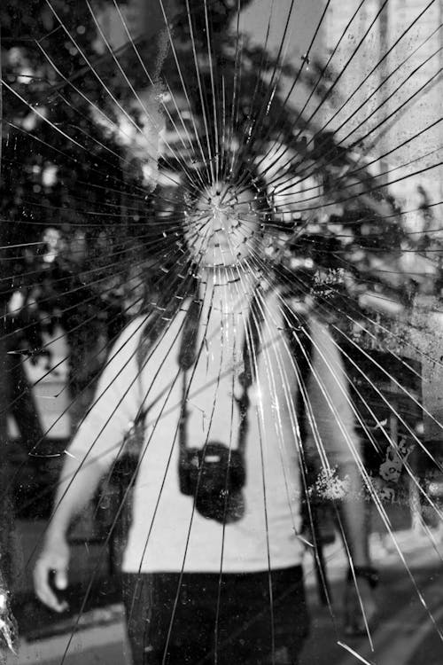 A man with a camera in his hand is standing in front of a broken glass