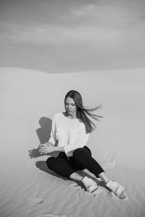 모래 언덕에 앉아 여자의 회색조 사진