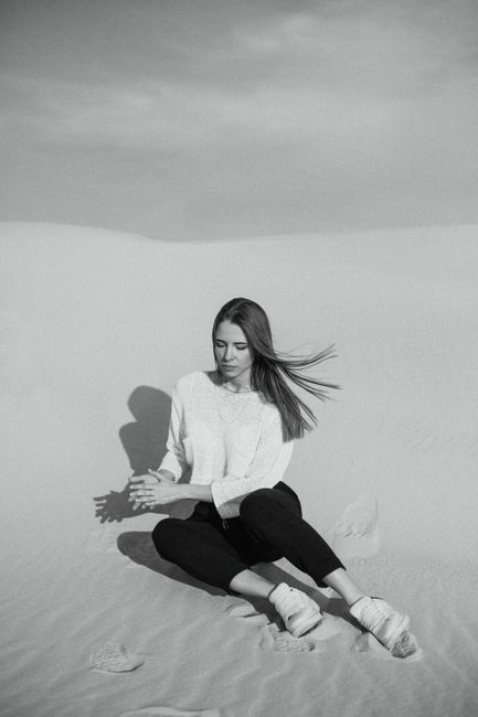 Portrait of a woman sitting in a tranquil desert scene, captured in black and white.