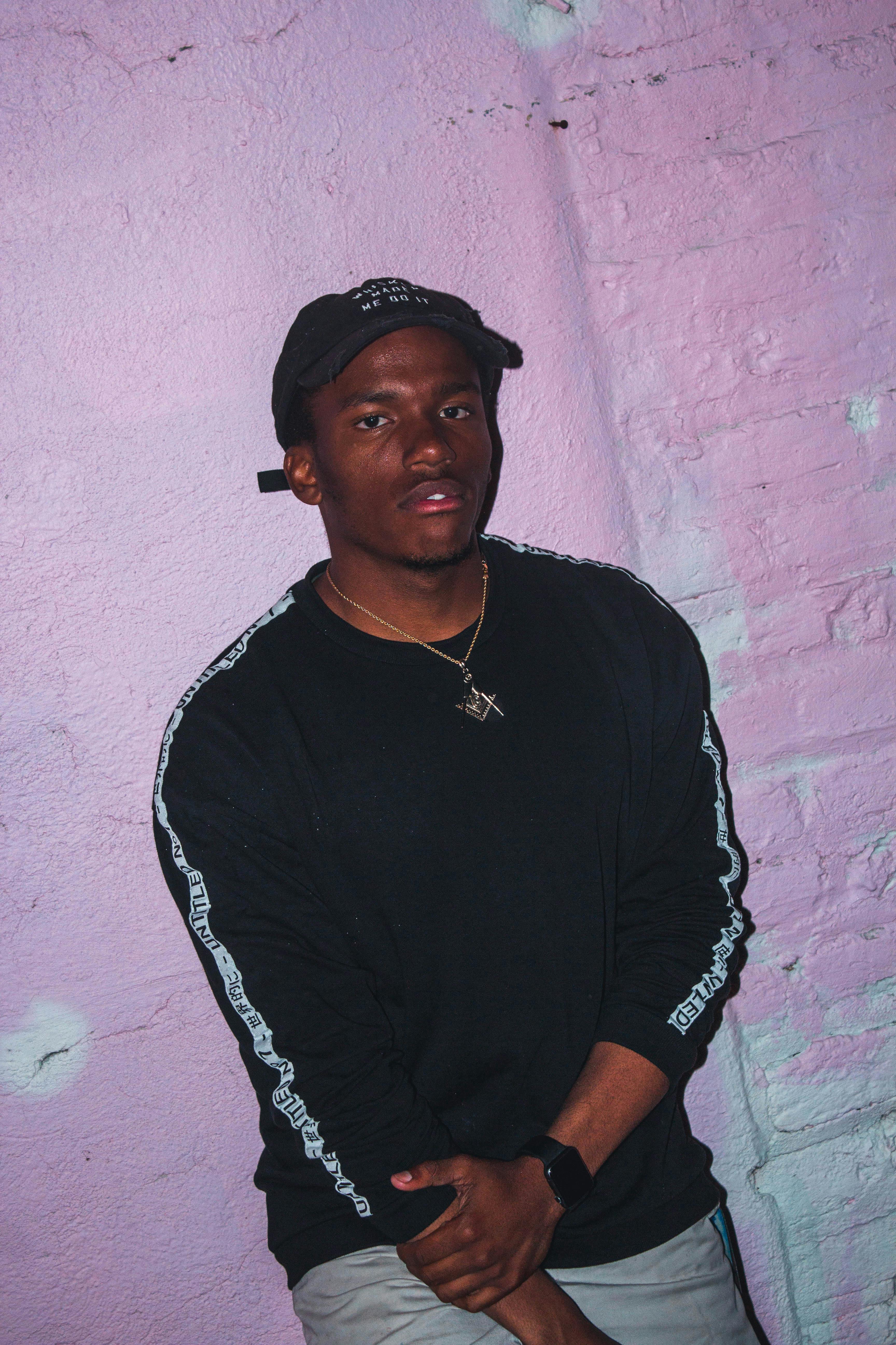 一名男子随意地靠在粉色城市墙壁上摆姿势，展现出自信的肖像