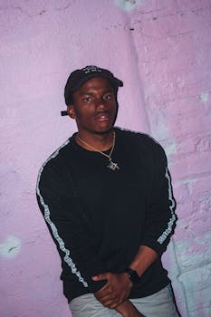 一名男子随意地靠在粉色城市墙壁上摆姿势，展现出自信的肖像