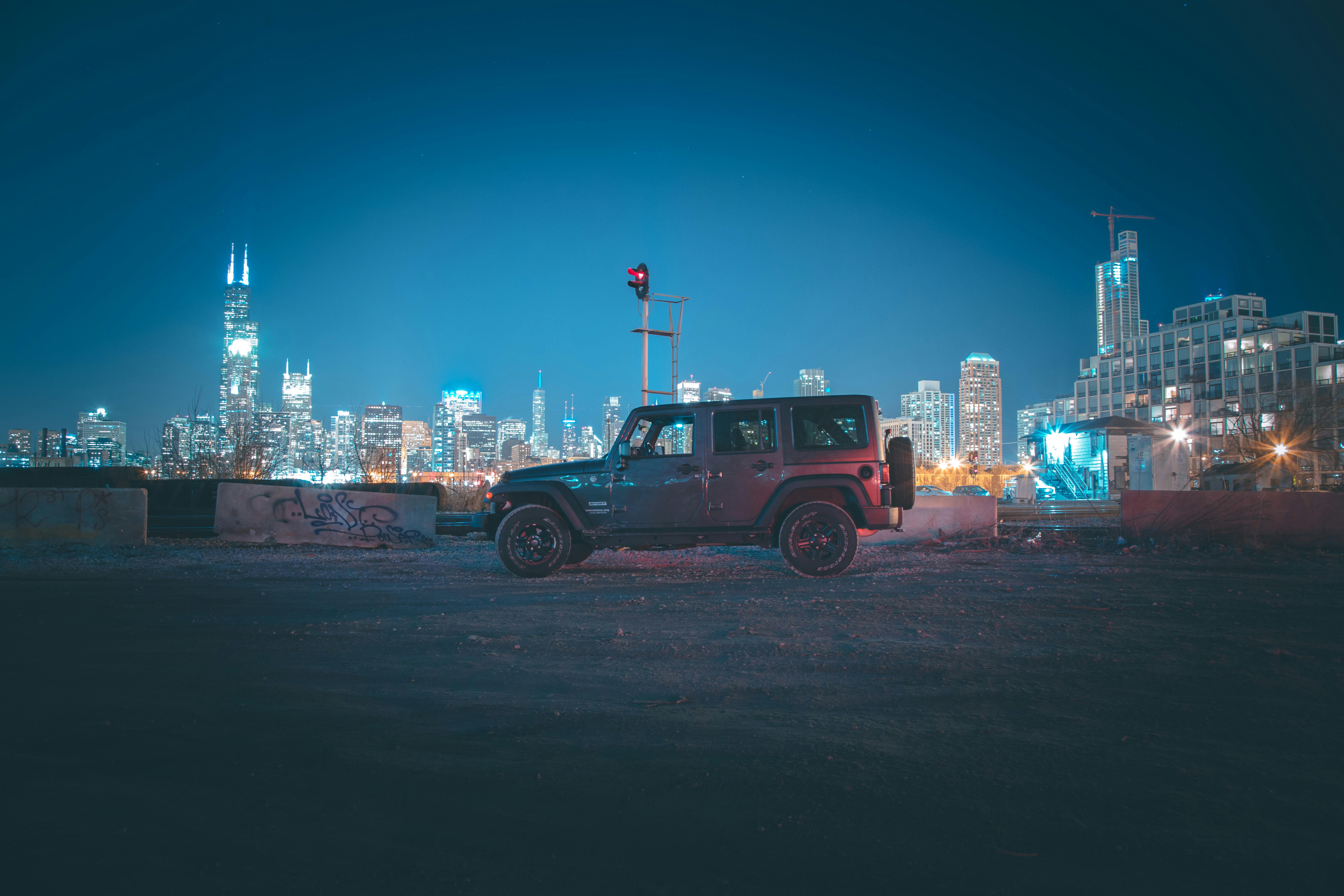 一辆吉普车停在夜晚的城市中，照亮的天际线捕捉到了城市的本质