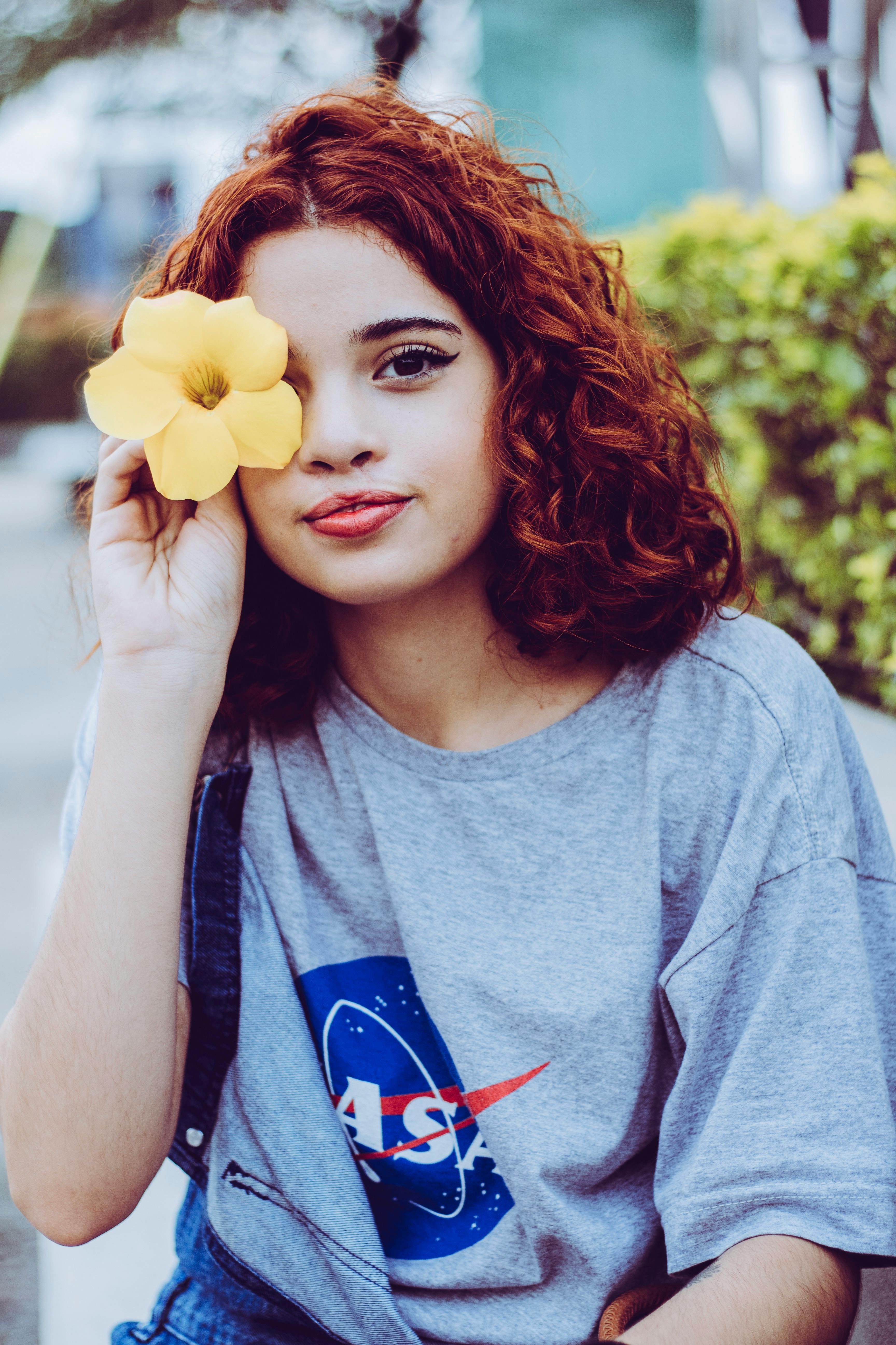 一位卷发的年轻女子在户外捧着一朵黄花，显得优雅又时尚