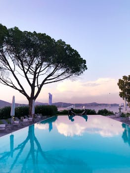 在宁静的黎明，无边泳池映照着热带环境中的树木和天空