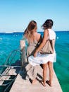 两个女人在蓝色海洋的码头上放松，拥抱夏日休闲