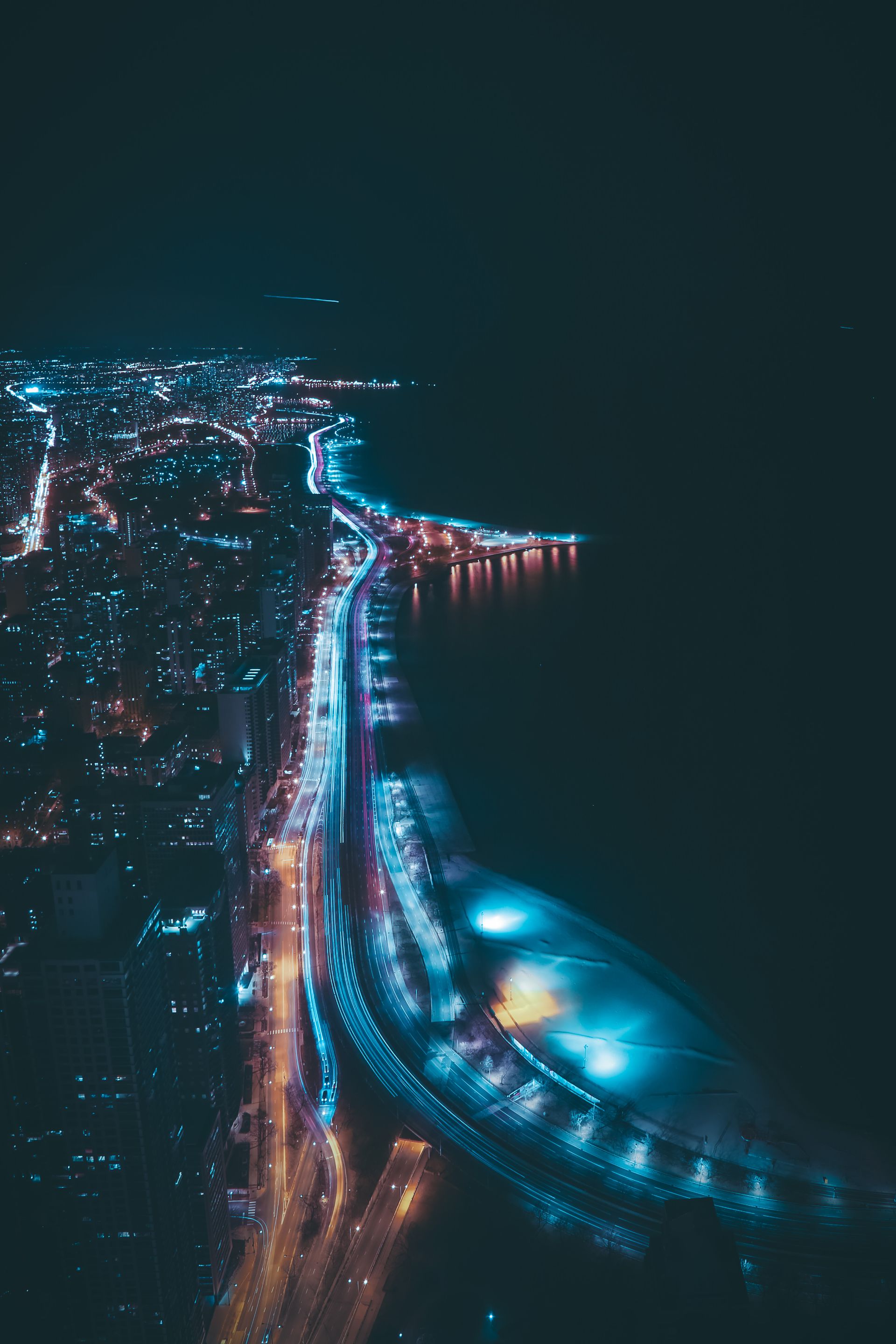 A stunning aerial view of Chicago's skyline at night, featuring dynamic light trails along the highway.