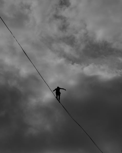 Фотография человека, идущего по канату, в оттенках серого под низким углом
