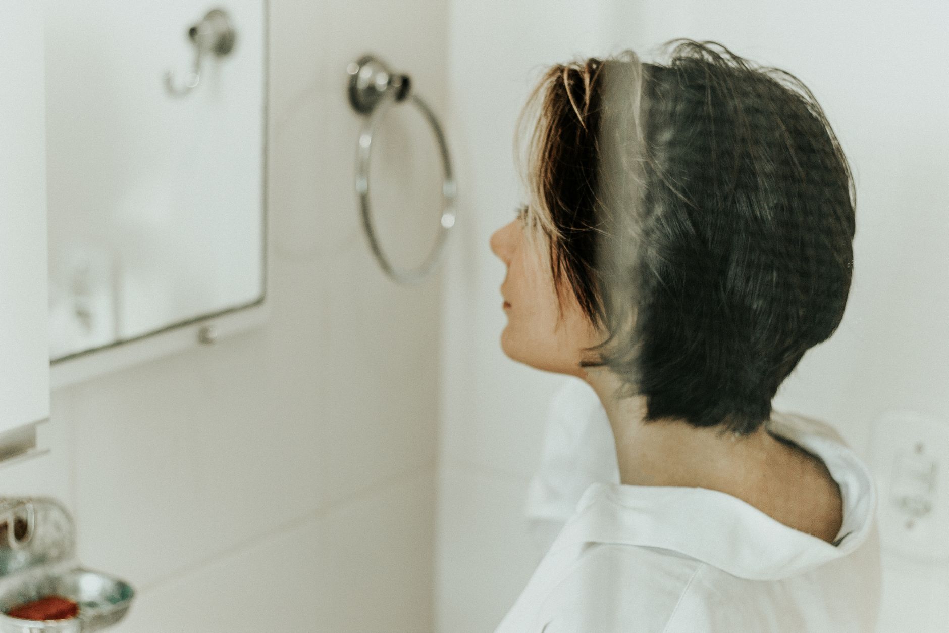 Profile view of a woman looking into a bathroom mirror, reflecting the uncertainty many readers feel when hair starts thinning.