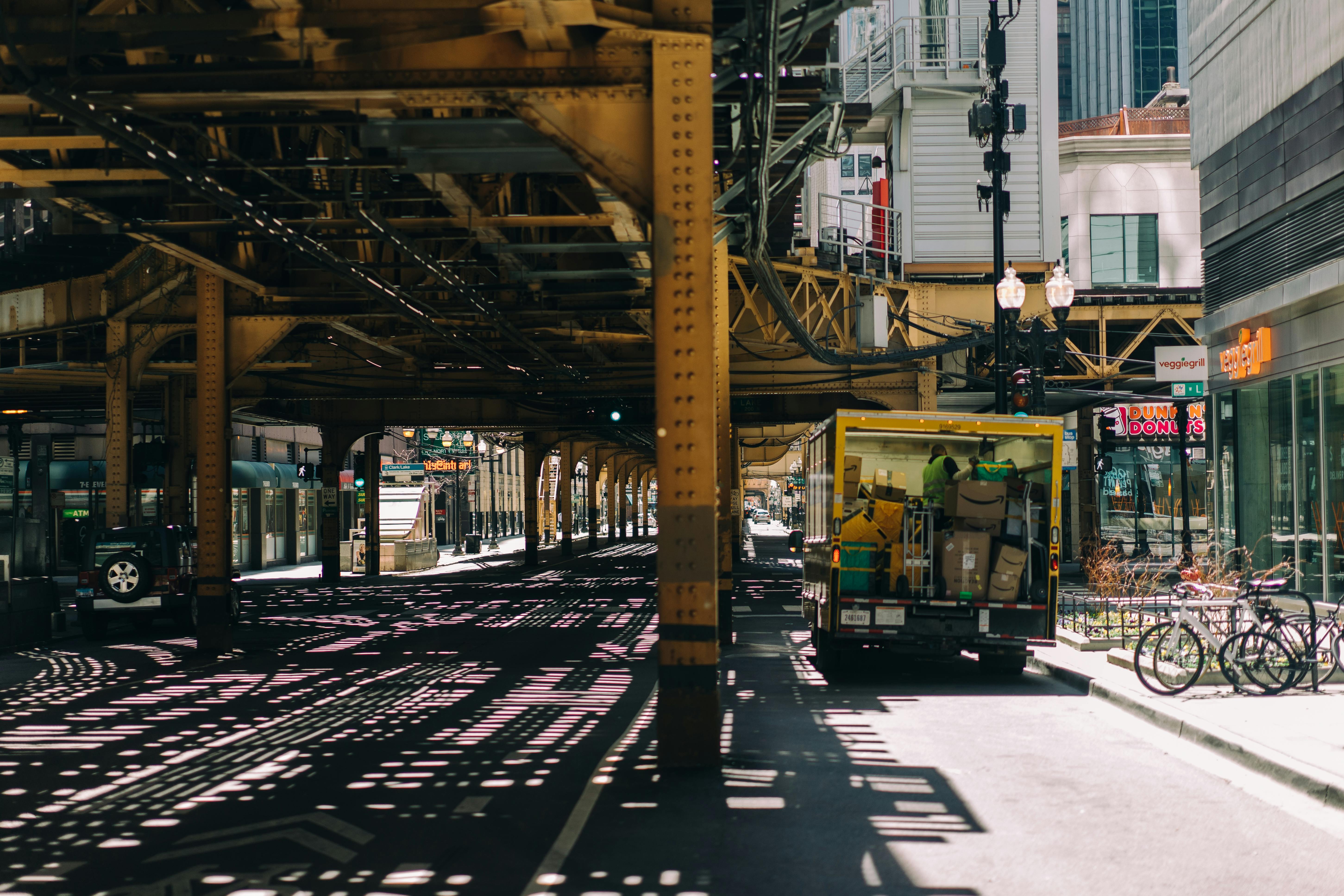 A busy Chicago street under elevated tracks with a delivery truck and bicycles, showcasing urban life.
