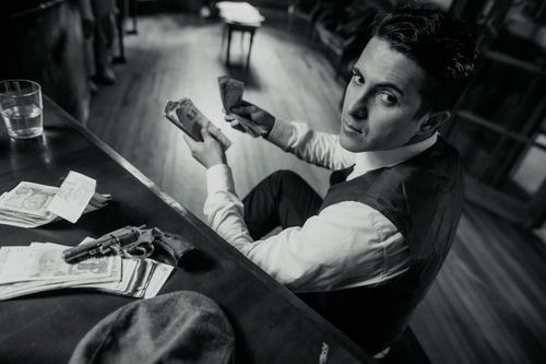 Free A man counting money with a gun on the desk in a vintage, mafia-themed setting. Stock Photo