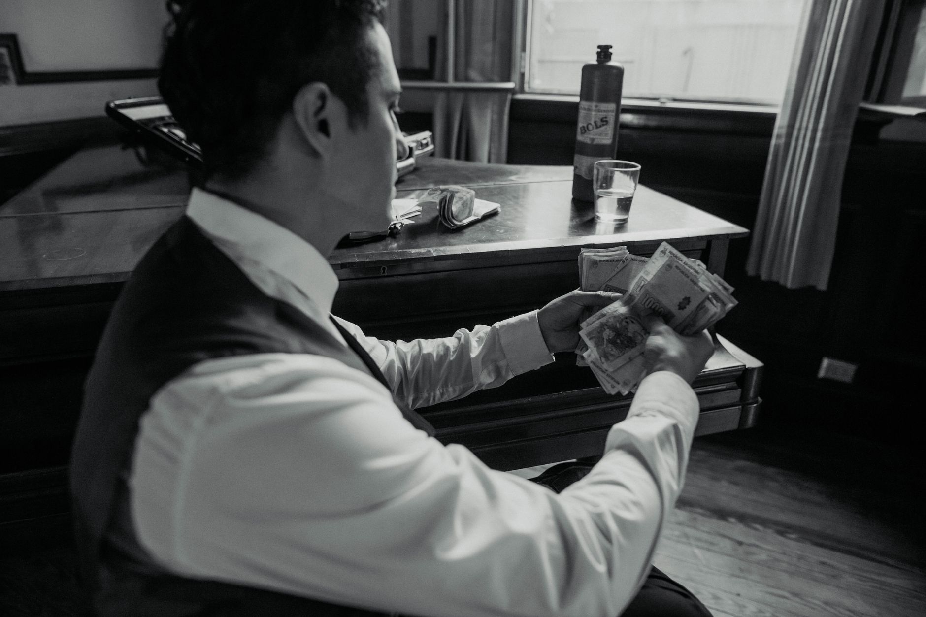 A man sits indoors counting Argentine pesos, captured in a black and white vintage style.