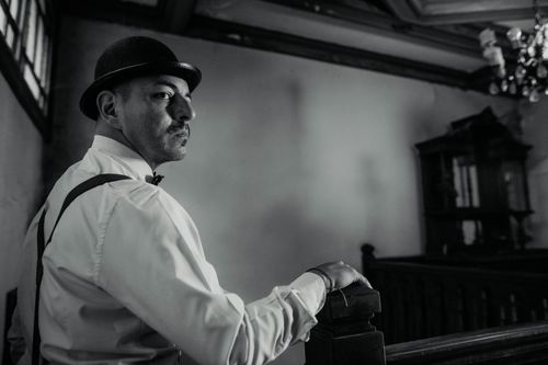 Free Classic black and white portrait of a man in a bowler hat standing by a wooden staircase in Buenos Aires. Stock Photo