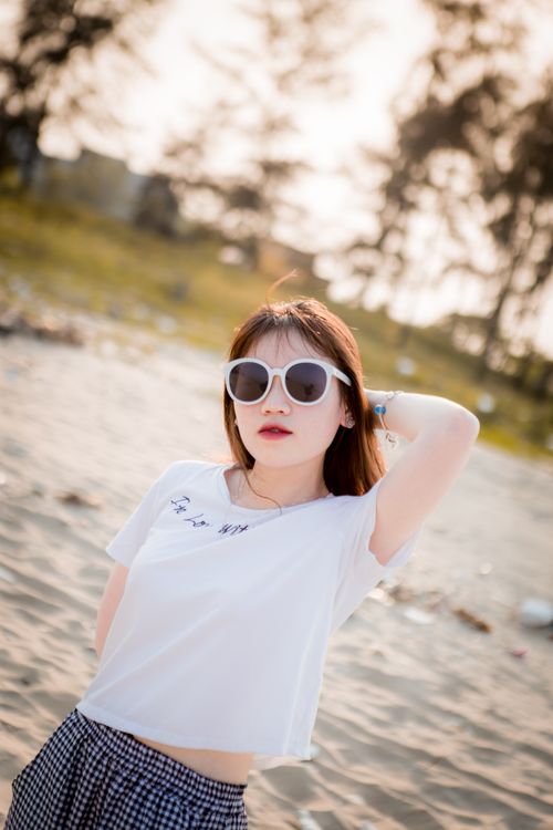 Free A stylish young woman with sunglasses posing confidently on a sunny beach. Stock Photo