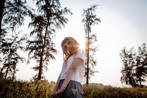 Free Stylish woman wearing sunglasses enjoys a sunny outdoor setting with trees. Stock Photo