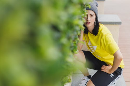 Photo of Woman in Adidas Outfit Squat Posing Beside Green Hedge