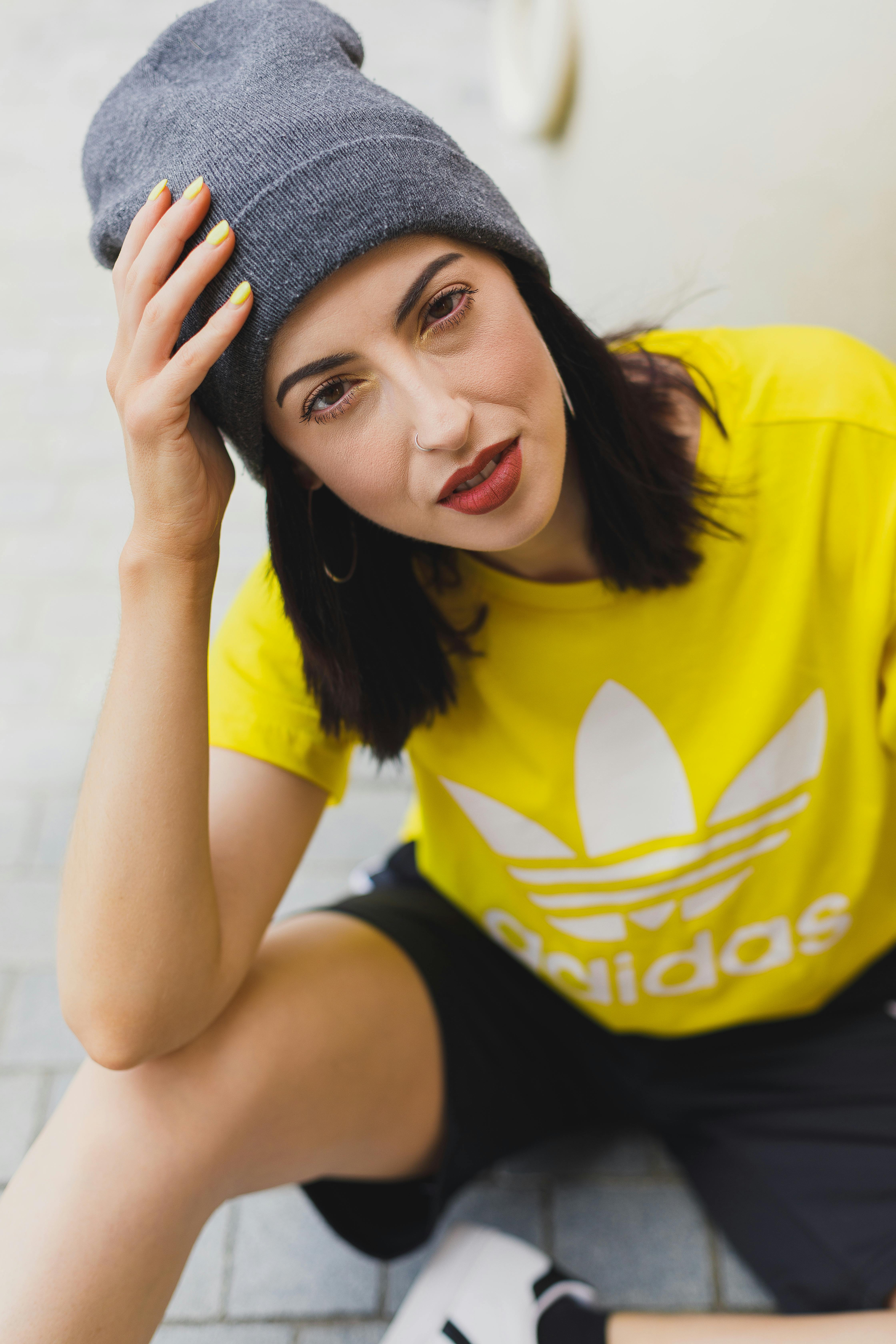 Stylish young woman in a yellow t-shirt and grey beanie sitting outdoors.