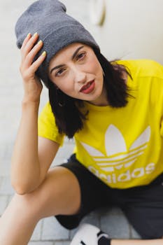 Stylish young woman in a yellow t-shirt and grey beanie sitting outdoors.