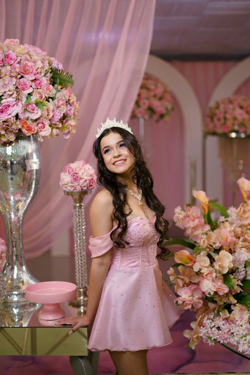 A young woman in a pink dress posing in front of a large floral arrangement