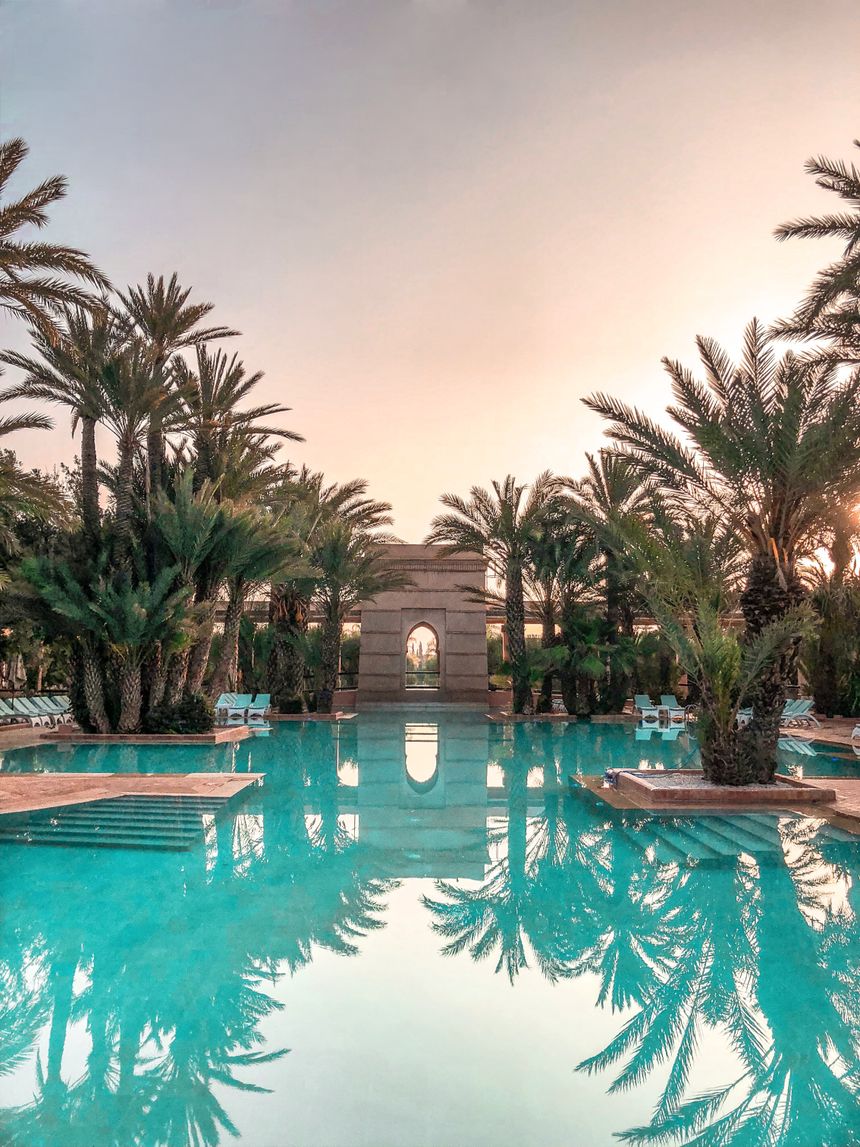 Palm-lined resort pool reflecting a sunset sky — photo by Vincent Rivaud on Pexels